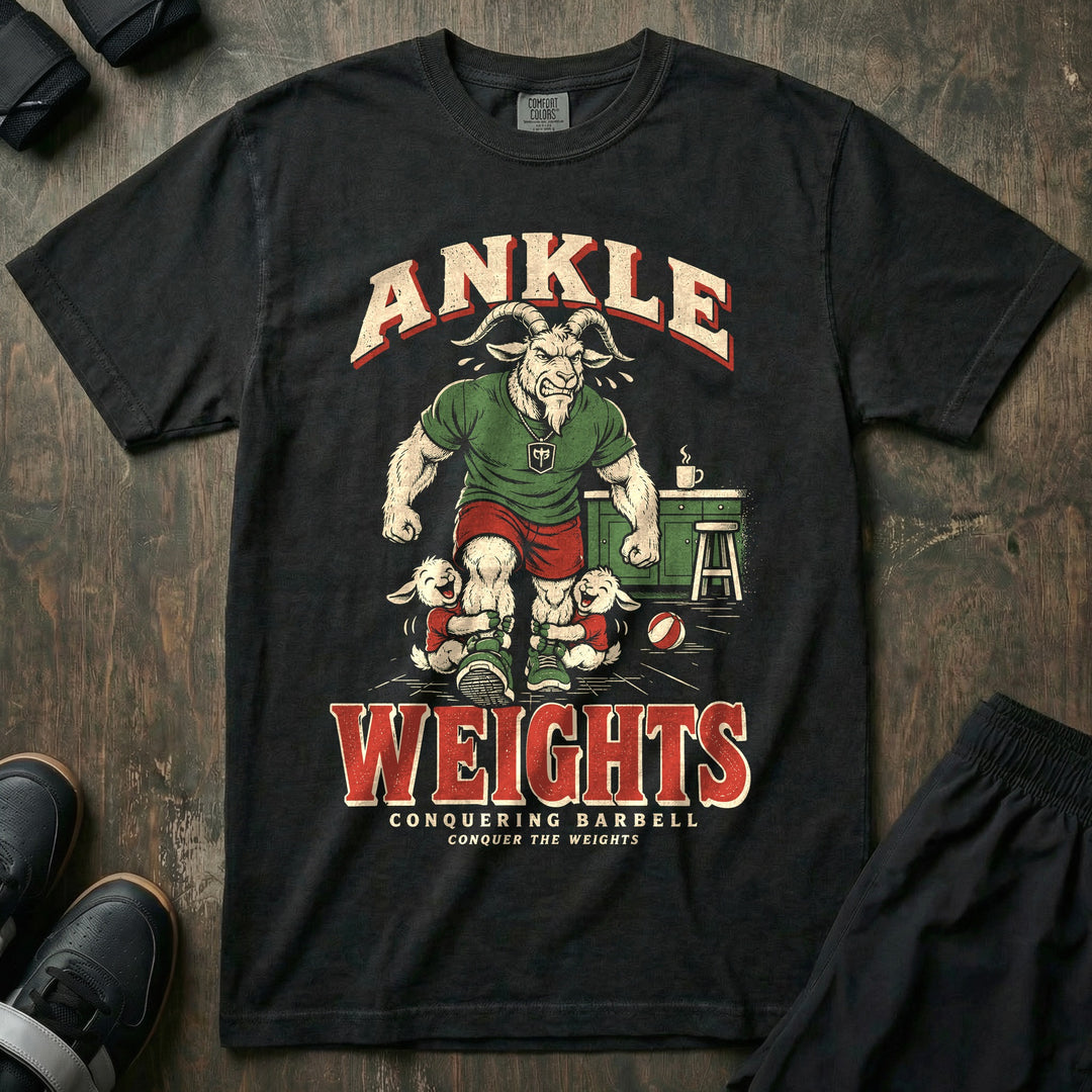 Ankle Weights - Relaxed Fit Tee front graphic in Black with a muscular goat dad walking through a kitchen with two laughing kid goats holding onto his ankles - Conquering Barbell