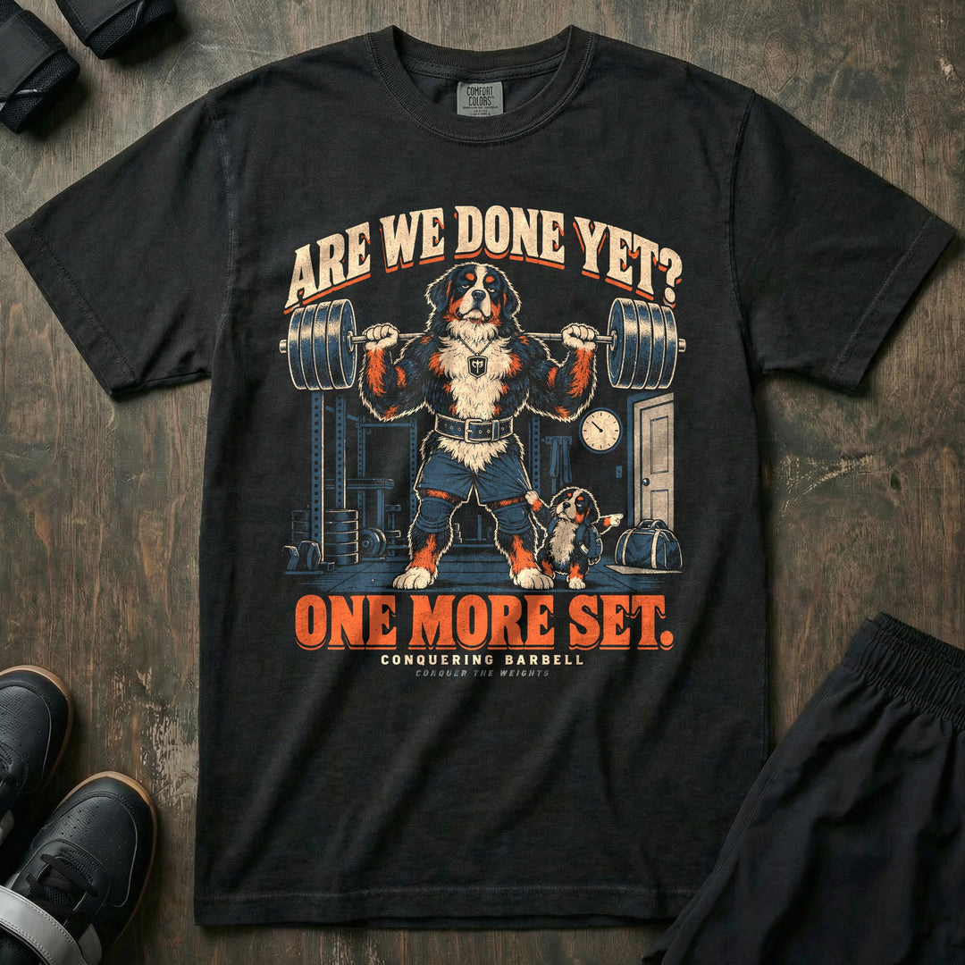 Are We Done Yet? One More Set - Relaxed Fit Tee front graphic in Black with a Bernese mountain dog dad with a loaded barbell on his back while a puppy tugs his shorts and points at the door - Conquering Barbell