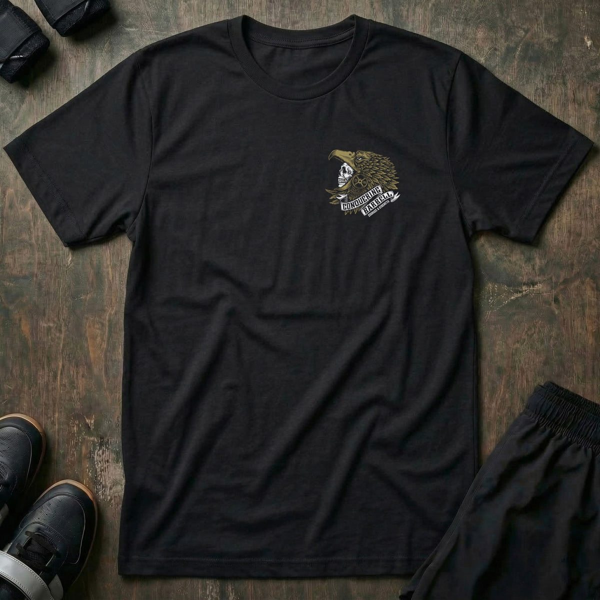 Aztec Eagle Warrior tee in Black: a skull warrior in a gold-feathered eagle headdress with a CONQUERING BARBELL ribbon banner