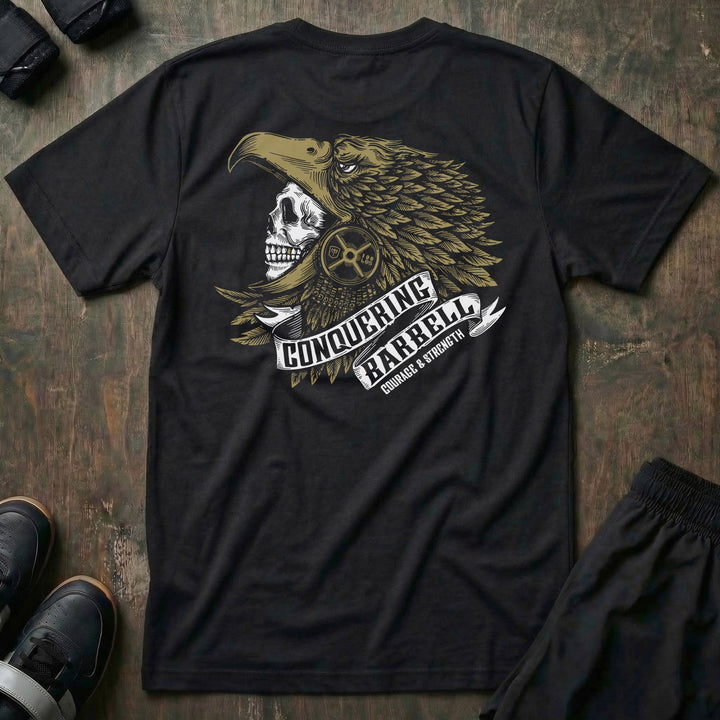 Aztec Eagle Warrior tee in Black: a skull warrior in a gold-feathered eagle headdress with a CONQUERING BARBELL ribbon banner