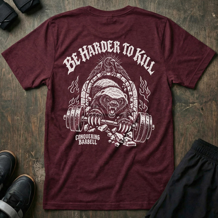 Be Harder to Kill Honey Badger tee in Maroon: a snarling honey badger bursting through a stone arch with a loaded barbell