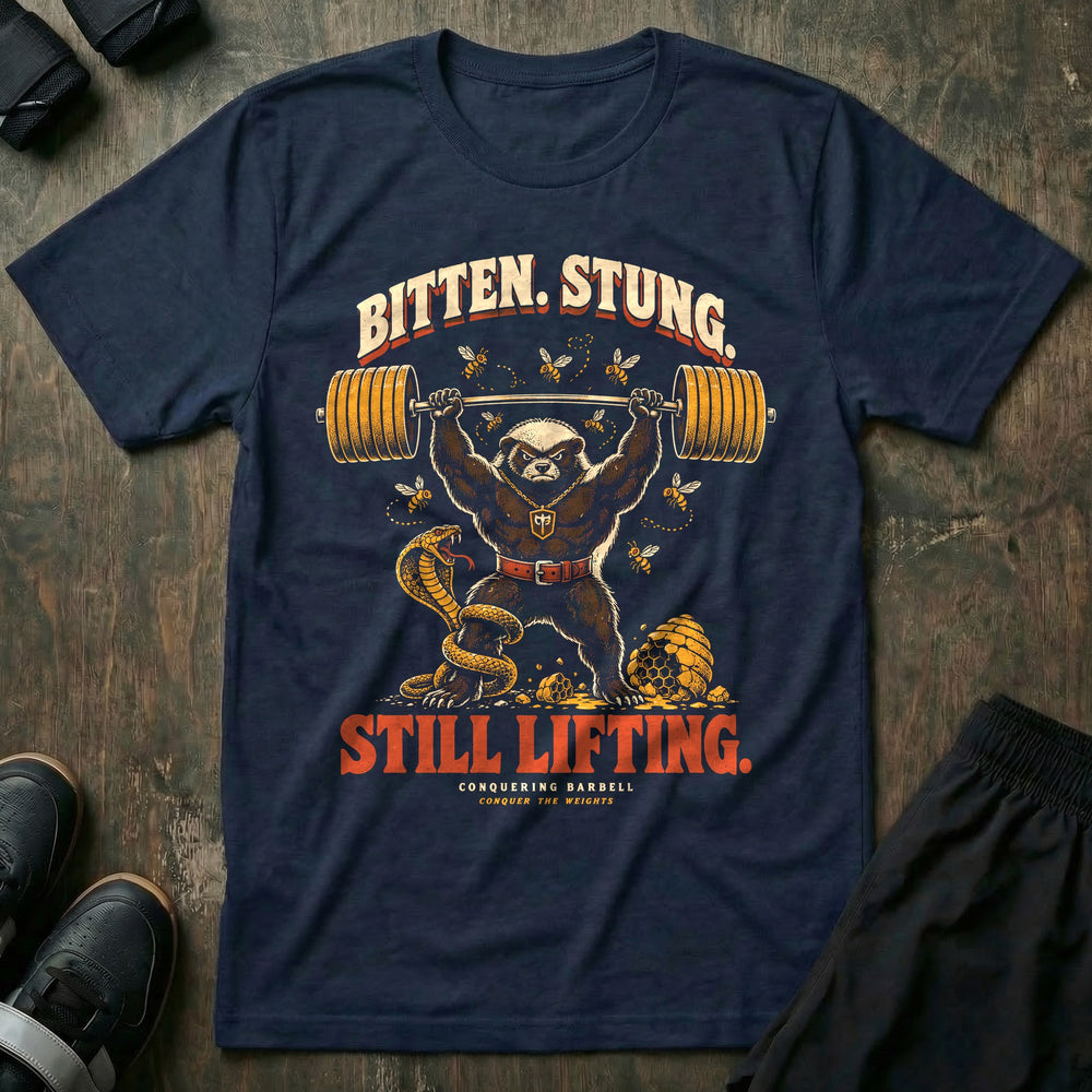Bitten Stung Still Lifting - Tee front graphic in Navy with a honey badger pressing a barbell overhead while bees swarm and a cobra coils - Conquering Barbell