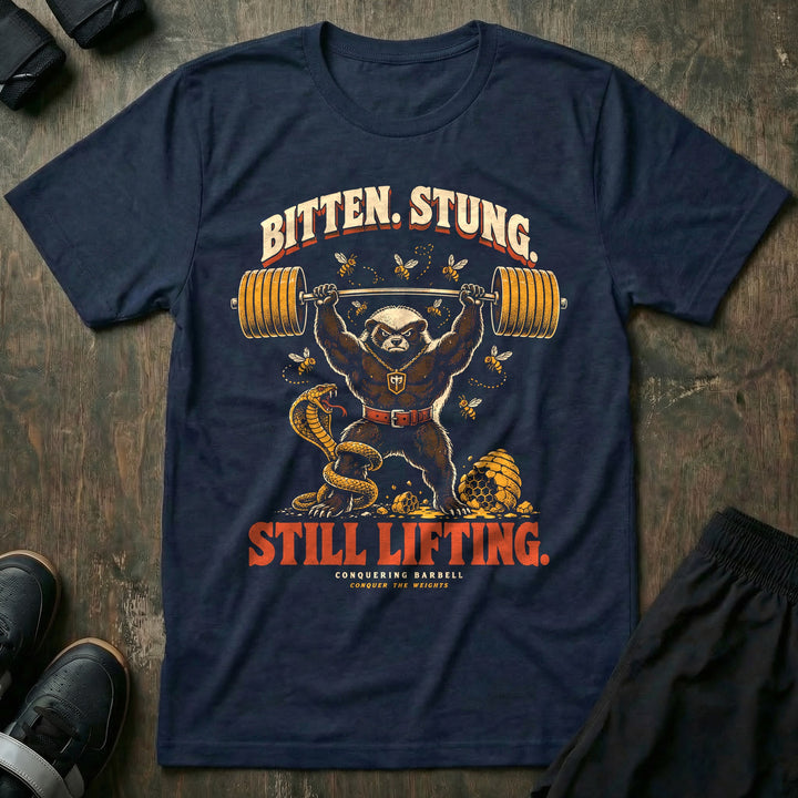 Bitten Stung Still Lifting - Tee front graphic in Navy with a honey badger pressing a barbell overhead while bees swarm and a cobra coils - Conquering Barbell