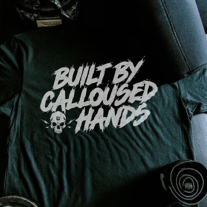 Built by Calloused Hands tee in Black: BUILT BY CALLOUSED HANDS in raw white brush lettering with a small skull