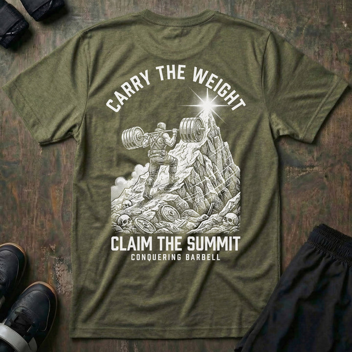 Carry the Weight, Claim the Summit tee in Military: an armored lifter hauling a loaded barbell up a jagged mountain toward