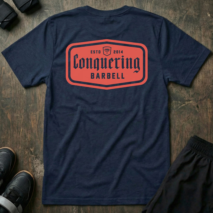 CB Iconic Label tee in Navy: a bold red CONQUERING BARBELL label badge with the CB shield and ESTD 2014 across the back