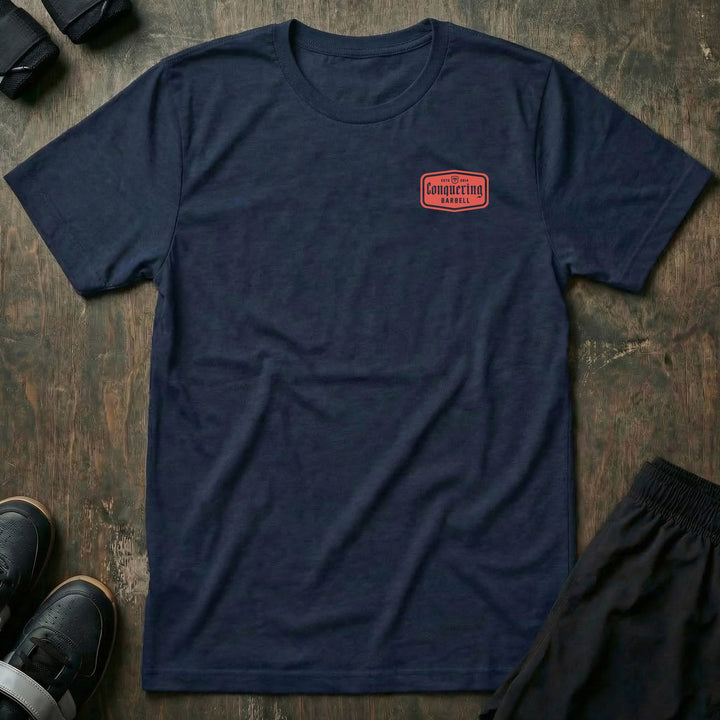 CB Iconic Label tee in Navy: a bold red CONQUERING BARBELL label badge with the CB shield and ESTD 2014 across the back