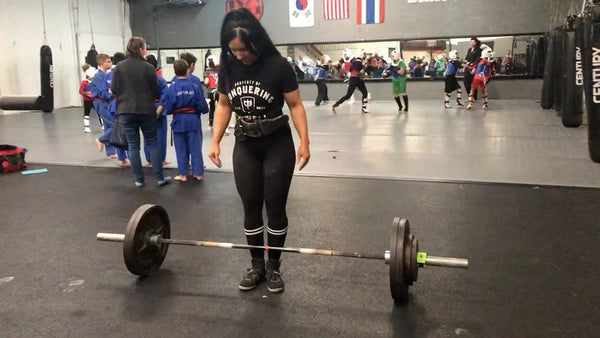 @britttlifts with a loaded deadlift bar in a Conquering Barbell tee