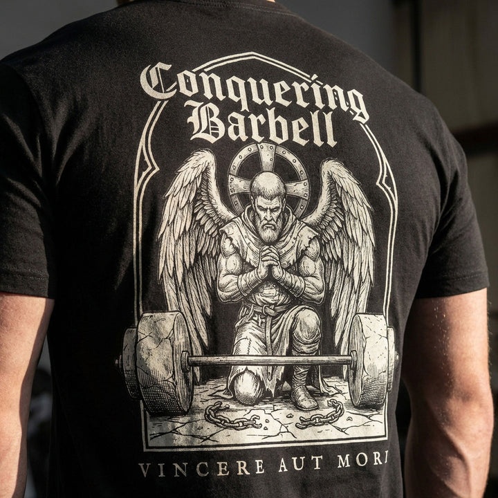 Conquer or Die Monk tee in Black: a winged warrior angel kneeling over a barbell inside a gothic archway