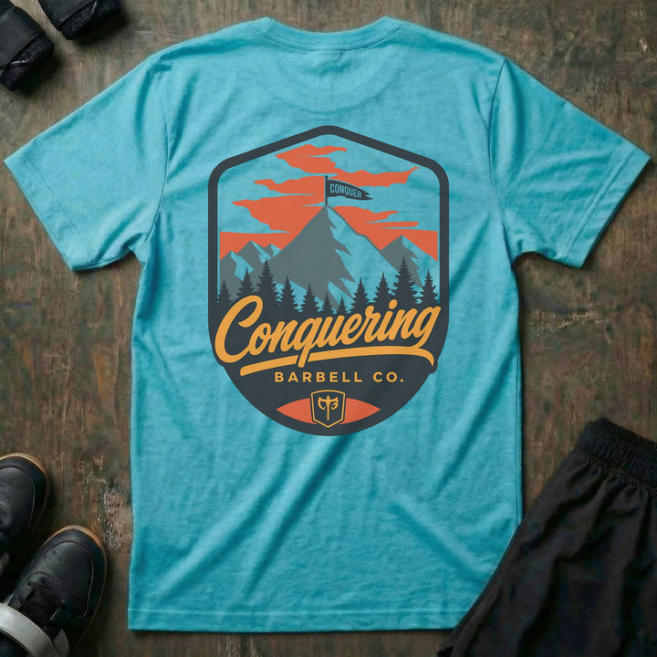 Conquer the Summit tee in Tahiti: a bold outdoor badge with snow-capped peaks above a pine tree line