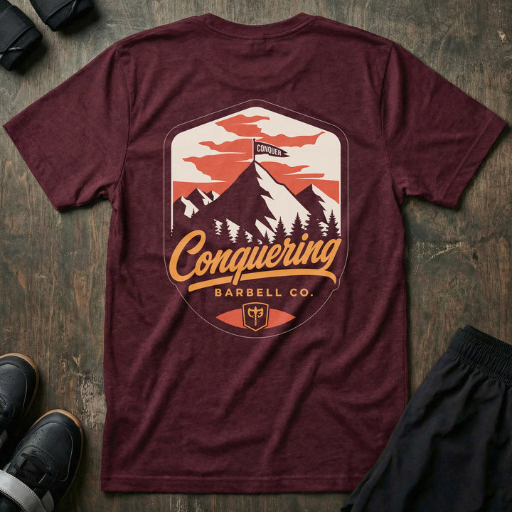 Conquer the Summit tee in Maroon: a bold outdoor badge with snow-capped peaks above a pine tree line