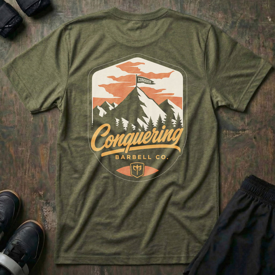 Conquer the Summit tee in Military: a bold outdoor badge with snow-capped peaks above a pine tree line