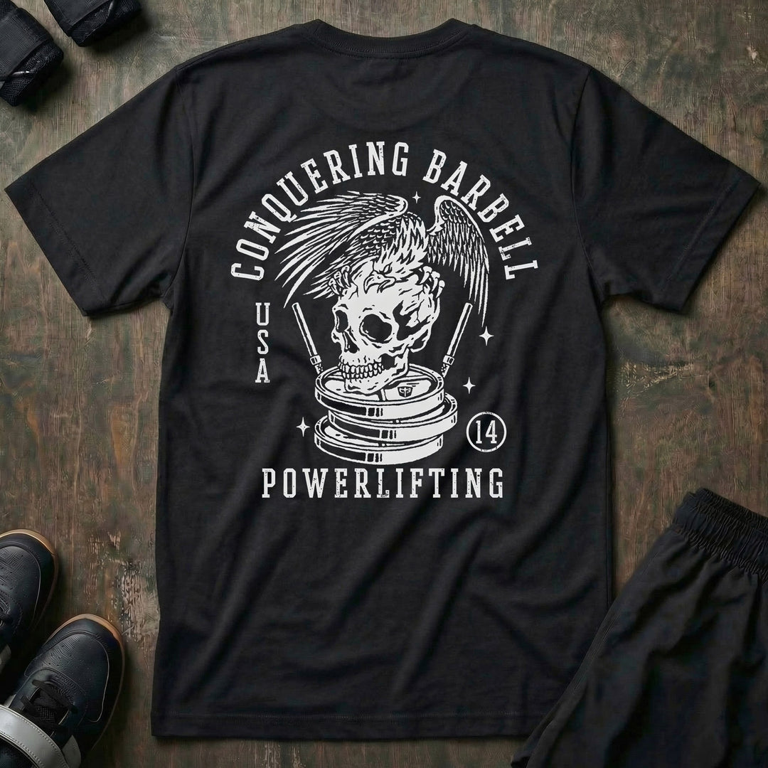 Conquering Barbell Eagle tee in Black: an eagle with spread wings perched on a skull atop stacked plates