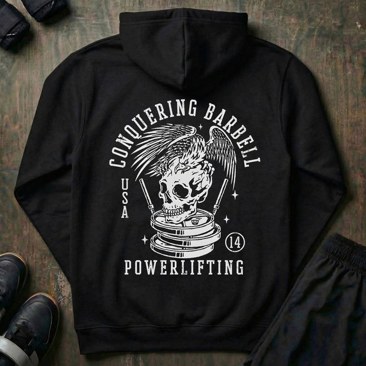 Conquering Barbell Eagle pullover hoodie in Black: spread wings over a skull perched on stacked plates with twin barbells