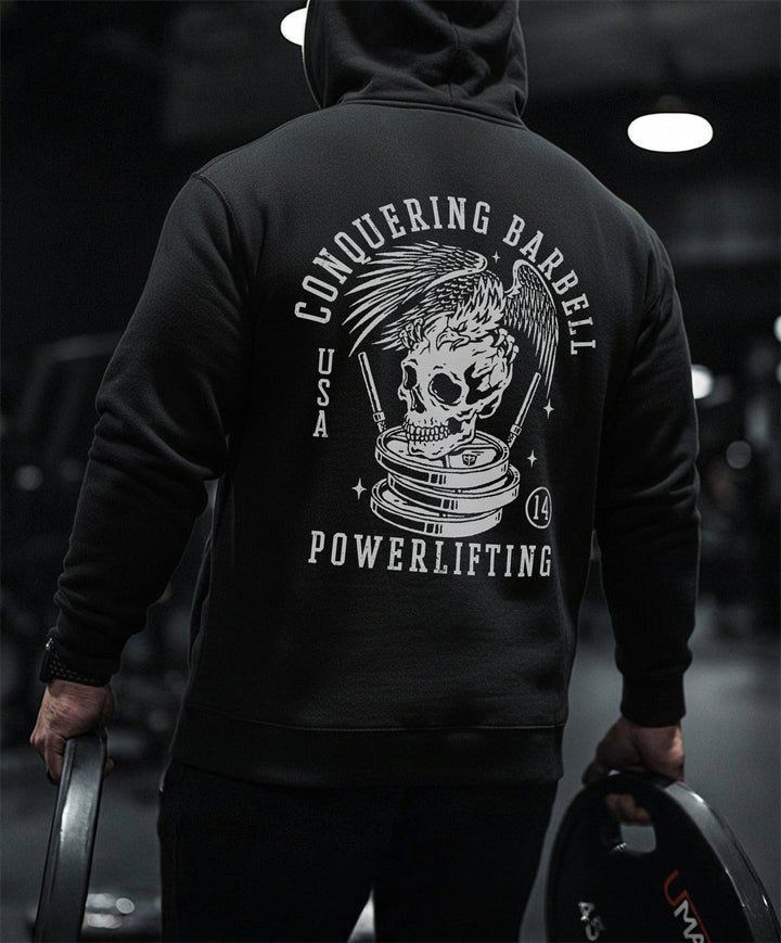 Conquering Barbell Eagle pullover hoodie in Black: spread wings over a skull perched on stacked plates with twin barbells