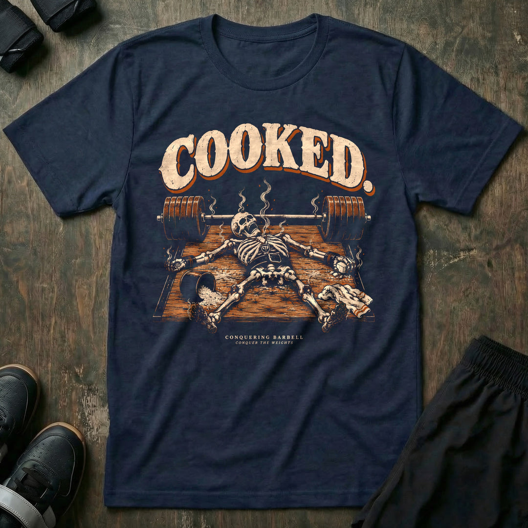 Cooked - Tee front graphic in Navy with a smoking skeleton laid out flat on the platform beside a loaded barbell - Conquering Barbell