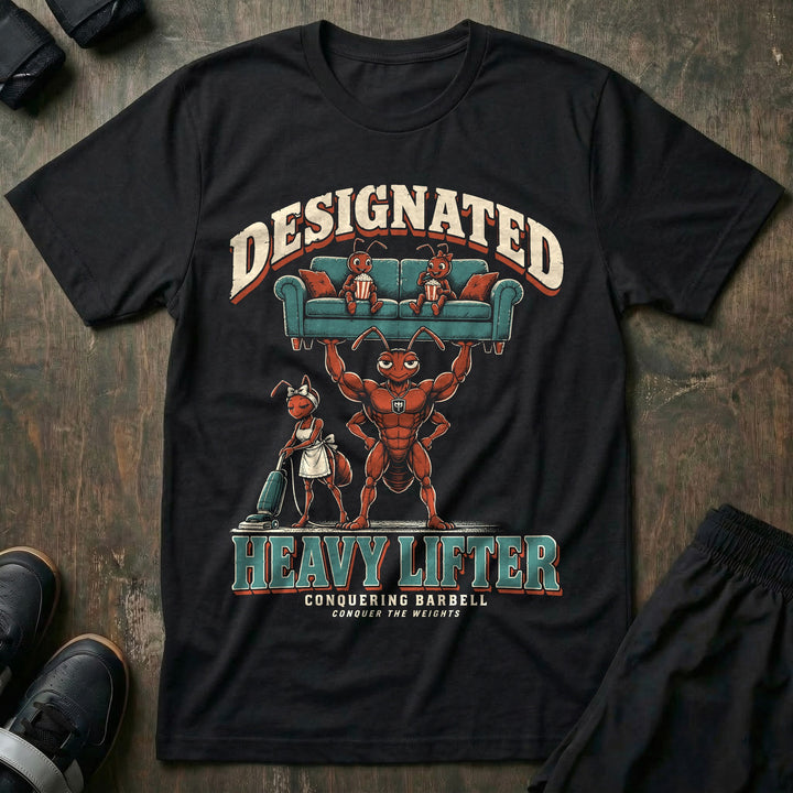 Designated Heavy Lifter - Tee front graphic in Black with a muscular ant dad lifting a couch overhead with two young ants eating popcorn on it while another ant vacuums below - Conquering Barbell