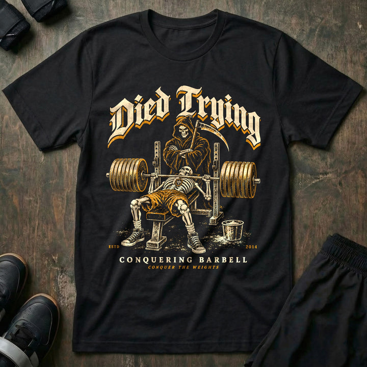 Died Trying - Tee front graphic in Black with a skeleton pinned under a loaded bar on the bench while the Grim Reaper stands behind the rack with his arms crossed - Conquering Barbell