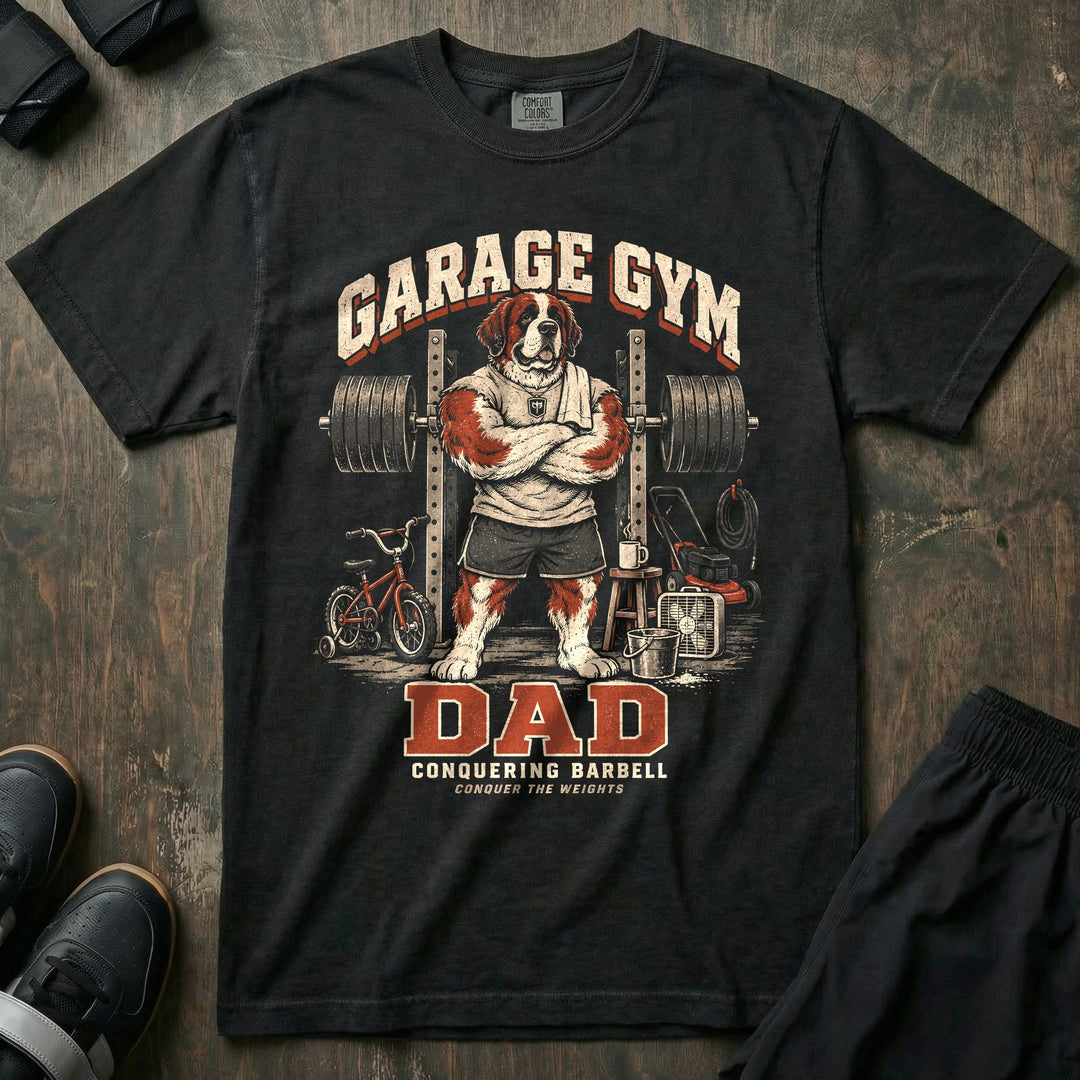 Garage Gym Dad - Relaxed Fit Tee front graphic in Black with a Saint Bernard dad with arms crossed in front of a loaded squat rack in a garage with a kid's bike and lawn mower - Conquering Barbell