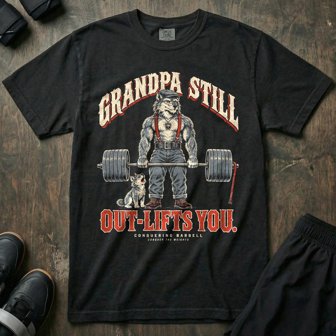 Grandpa Still Out-Lifts You - Relaxed Fit Tee front graphic in Black with a gray wolf grandpa in a flat cap and suspenders deadlifting a loaded barbell with a cane leaning on it and a wolf pup howling - Conquering Barbell