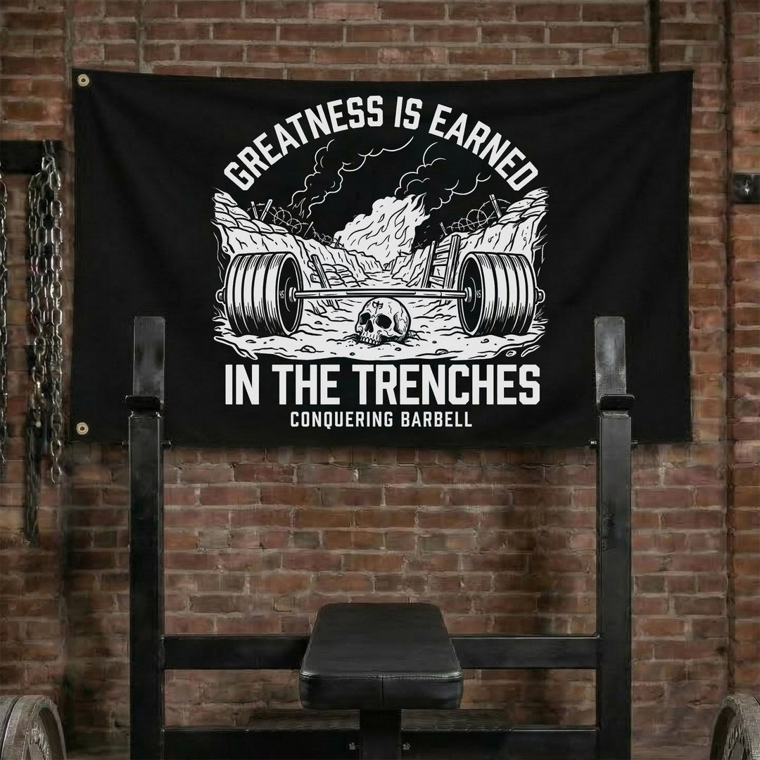 Greatness is Earned in the Trenches - Polyester Flag, horizontal black gym flag with loaded barbell dug into a trench below barbed wire - Conquering Barbell