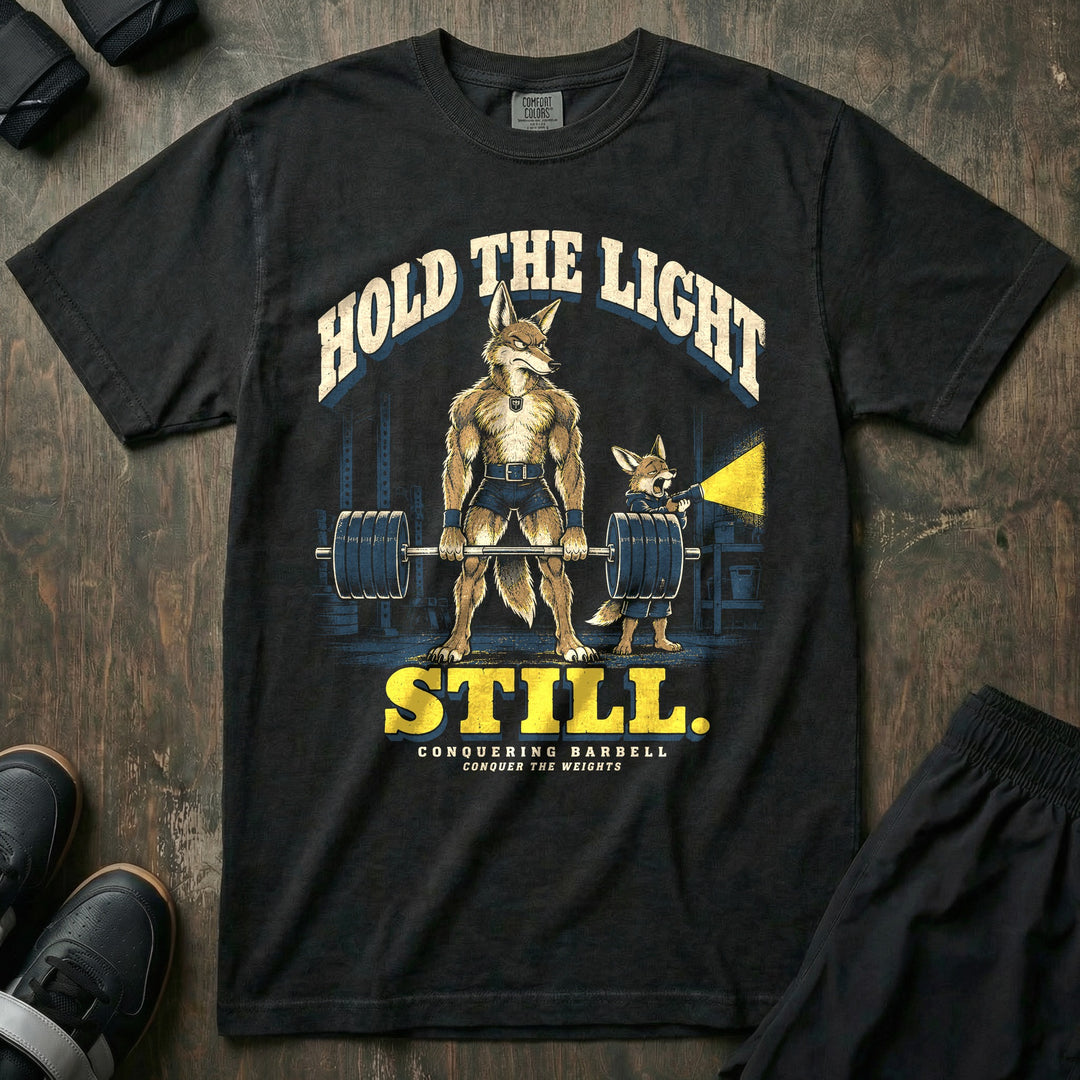 Hold the Light Still - Relaxed Fit Tee front graphic in Black with a coyote dad deadlifting a loaded barbell in a dark garage while a yawning coyote pup holds a flashlight - Conquering Barbell