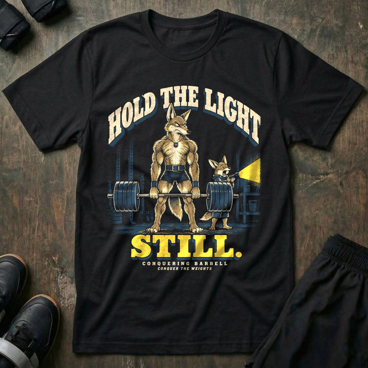 Hold the Light Still - Tee front graphic in Black with a coyote dad deadlifting a loaded barbell in a dark garage while a yawning coyote pup holds a flashlight - Conquering Barbell