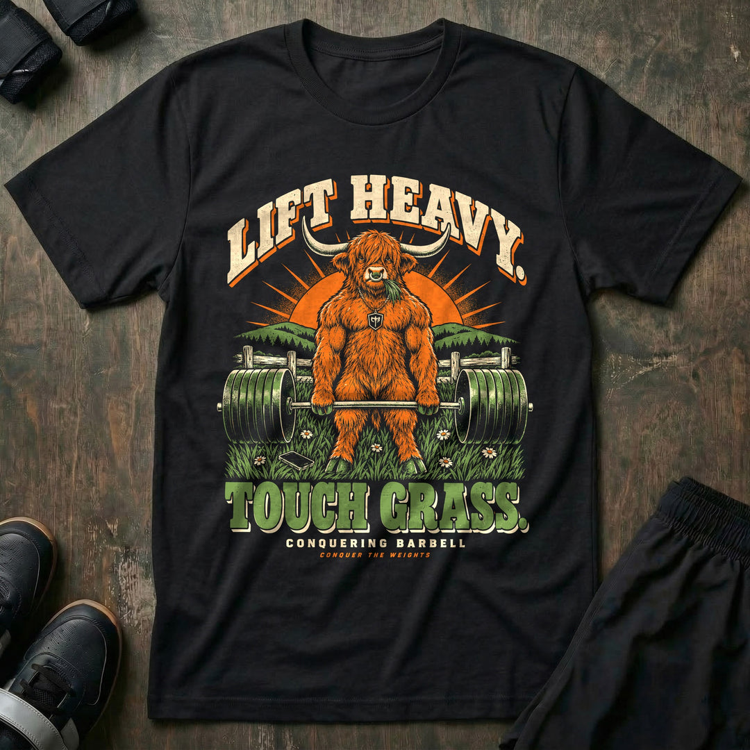 Lift Heavy Touch Grass - Tee front graphic in Black with a Highland bull chewing grass at deadlift lockout in a meadow - Conquering Barbell