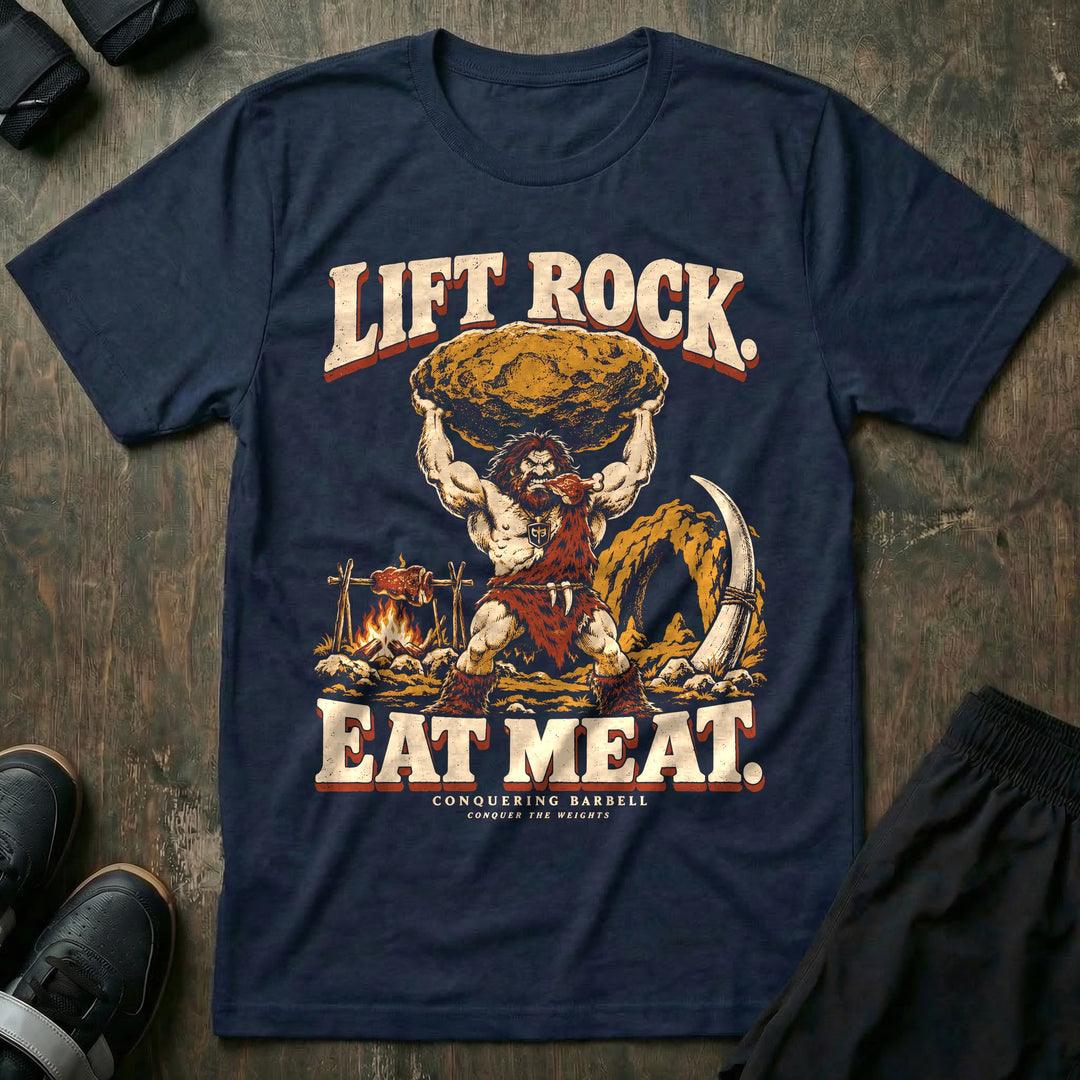 Lift Rock Eat Meat - Tee front graphic in Navy with a caveman holding a boulder overhead beside meat roasting on a spit - Conquering Barbell