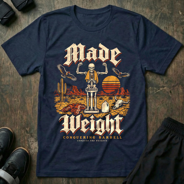 Made Weight - Tee front graphic in Navy with a skeleton flexing on a balance scale in the desert while vultures circle - Conquering Barbell