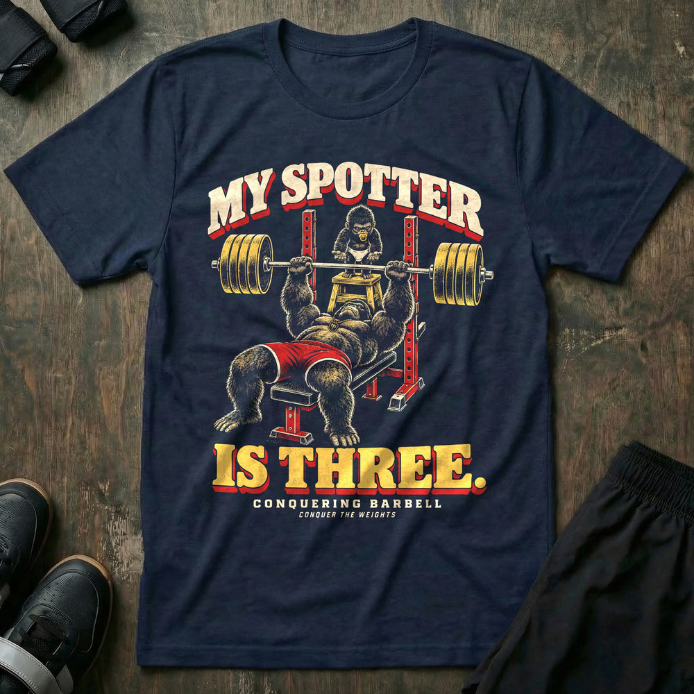 My Spotter Is Three - Tee front graphic in Navy with a gorilla dad bench pressing a loaded barbell while a baby gorilla in a diaper spots him from a step stool - Conquering Barbell