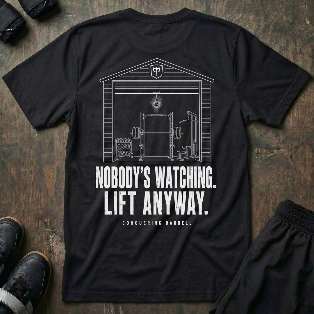 Nobody's Watching. Lift Anyway. tee in Black: a clean line illustration of a garage gym with a power rack