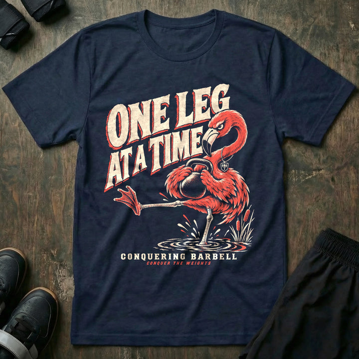One Leg at a Time - Tee front graphic in Navy with a flamingo balancing on one leg while holding a kettlebell - Conquering Barbell