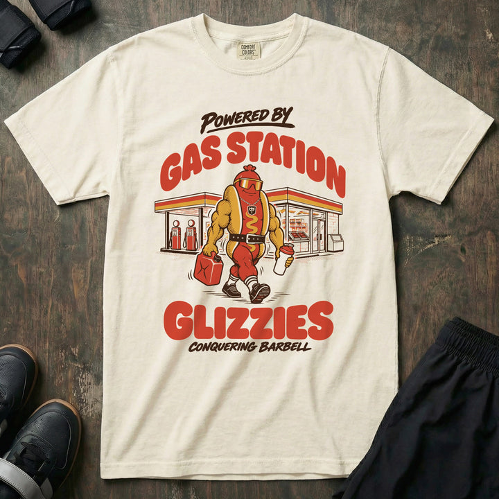 Powered by Gas Station Glizzies - Relaxed Fit Tee front graphic in Ivory with a muscular hot dog lifter walking out of a gas station under POWERED BY GAS STATION GLIZZIES - Conquering Barbell