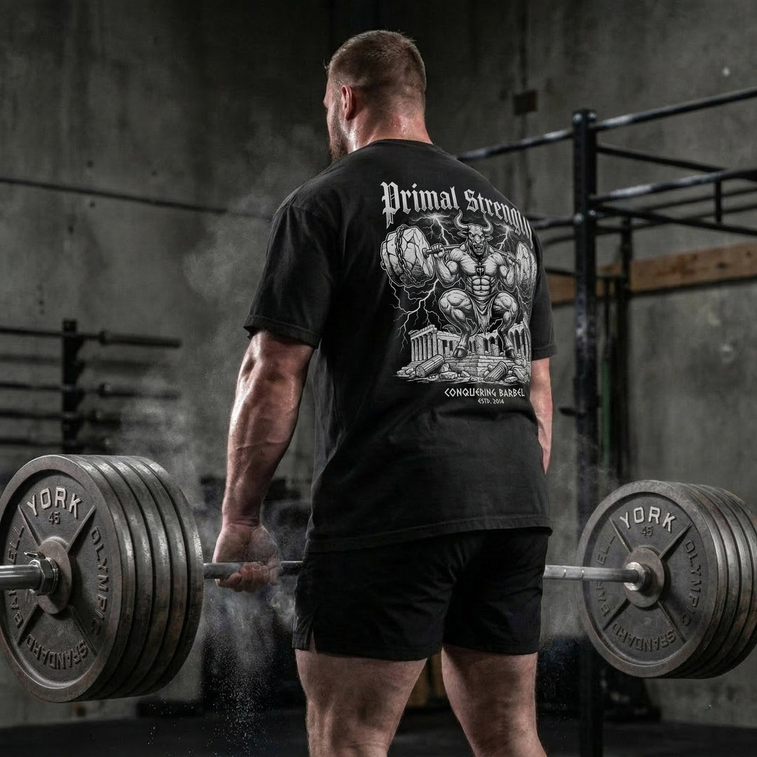 Primal Strength Minotaur relaxed fit tee in Black: a massive minotaur squatting a barbell loaded with boulder plates
