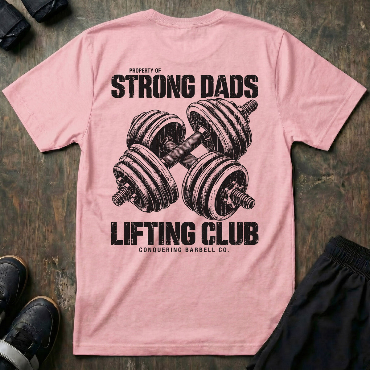 Property of Strong Dads Lifting Club tee in Pink: a pair of crossed dumbbells between PROPERTY OF STRONG DADS