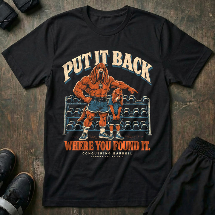 Put It Back Where You Found It - Tee front graphic in Black with a bloodhound dad pointing at a dumbbell rack while a young bloodhound holds a dumbbell with his head down - Conquering Barbell