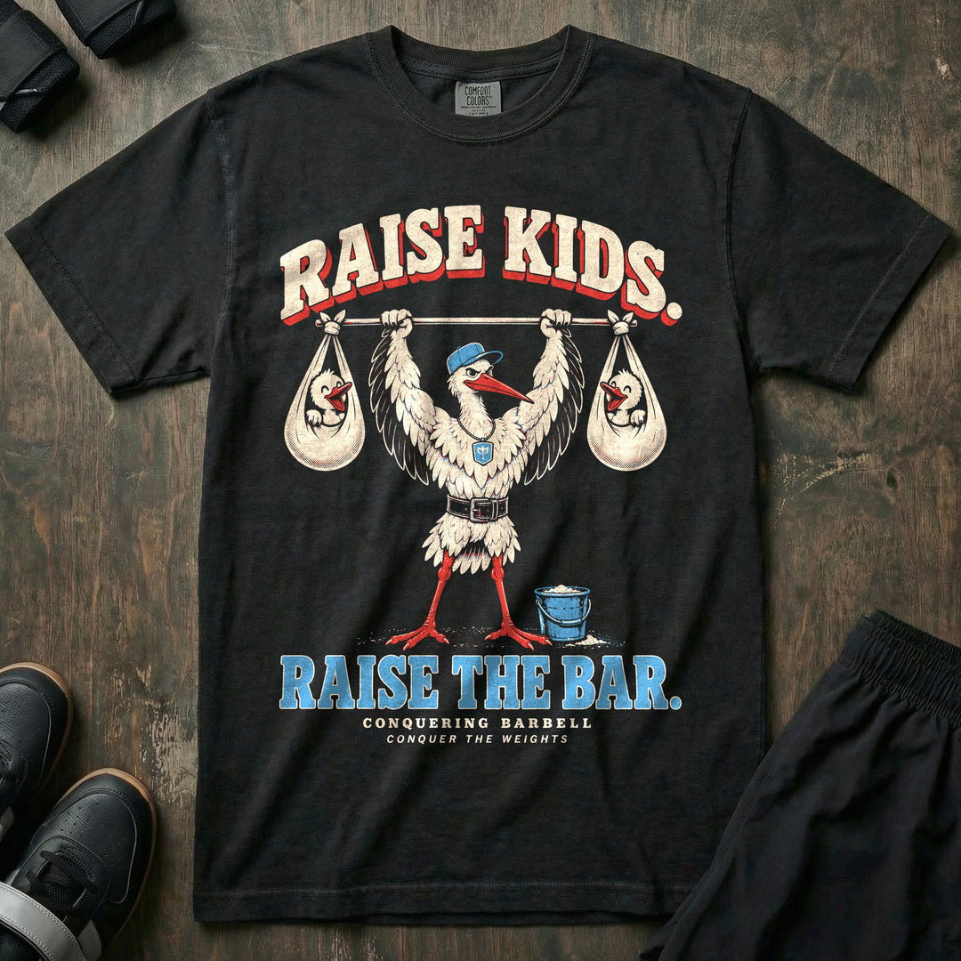 Raise Kids. Raise the Bar - Relaxed Fit Tee front graphic in Black with a stork dad in a ball cap pressing a barbell overhead with a baby bundle hanging from each end - Conquering Barbell