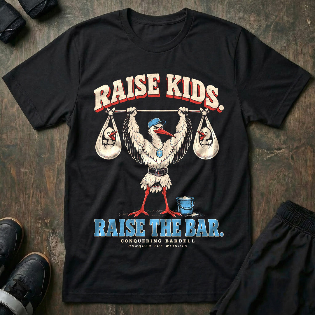 Raise Kids. Raise the Bar - Tee front graphic in Black with a stork dad in a ball cap pressing a barbell overhead with a baby bundle hanging from each end - Conquering Barbell