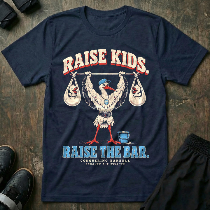 Raise Kids. Raise the Bar - Tee front graphic in Navy with a stork dad in a ball cap pressing a barbell overhead with a baby bundle hanging from each end - Conquering Barbell