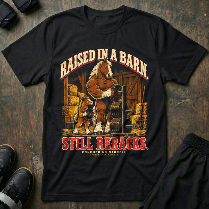 Raised in a Barn. Still Reracks - Tee front graphic in Black with a Clydesdale horse dad putting a weight plate on a rack in a barn while a foal carries another plate - Conquering Barbell