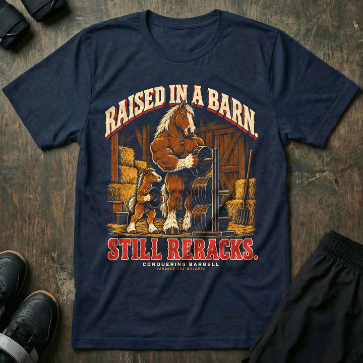 Raised in a Barn. Still Reracks - Tee front graphic in Navy with a Clydesdale horse dad putting a weight plate on a rack in a barn while a foal carries another plate - Conquering Barbell