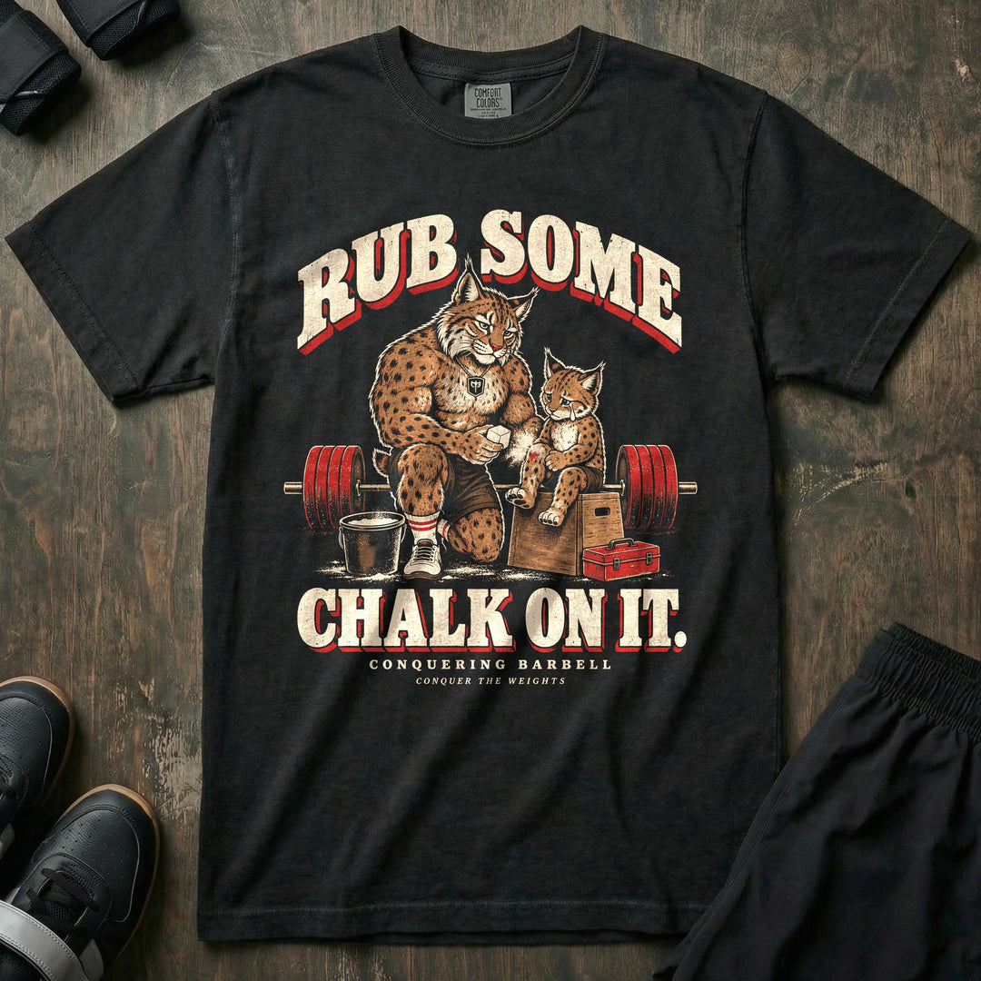 Rub Some Chalk on It - Relaxed Fit Tee front graphic in Black with a bobcat dad kneeling and rubbing chalk on the leg of a crying bobcat cub sitting on a wooden box - Conquering Barbell