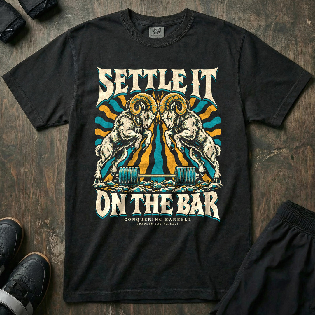 Settle It on the Bar - Relaxed Fit Tee front graphic in Black with two bighorn rams locking horns over a loaded barbell - Conquering Barbell