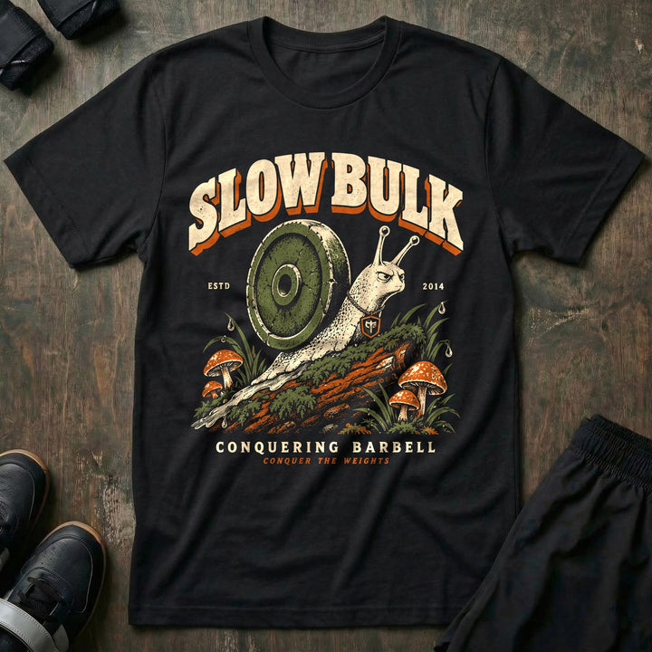 Slow Bulk - Tee front graphic in Black with a snail with a weight plate for a shell crossing a mossy log - Conquering Barbell