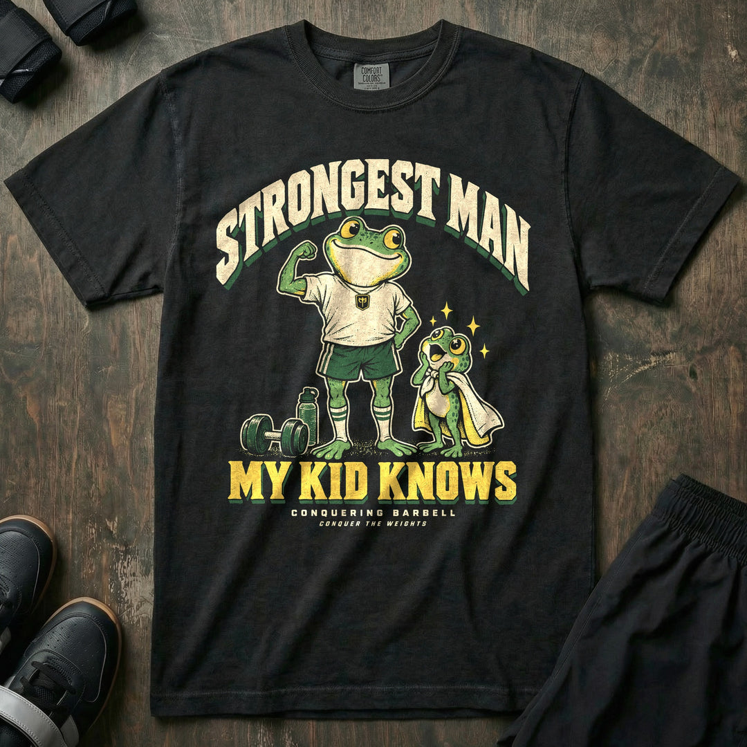 Strongest Man My Kid Knows - Relaxed Fit Tee front graphic in Black with a frog dad flexing one arm while a young frog in a towel cape looks up in awe - Conquering Barbell