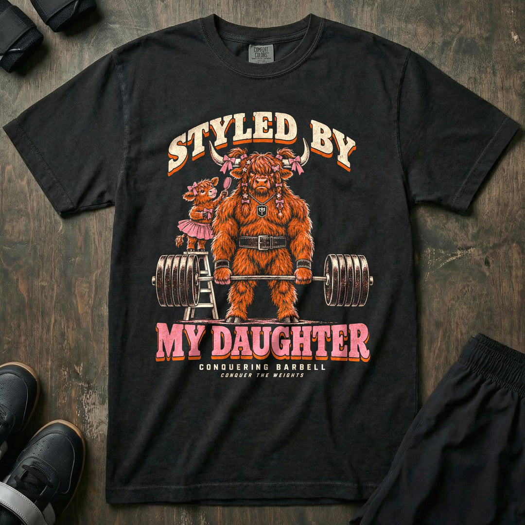 Styled by My Daughter - Relaxed Fit Tee front graphic in Black with a Highland bull dad with pink bows in his hair deadlifting a loaded barbell while his daughter in a tutu brushes his hair from a ladder - Conquering Barbell