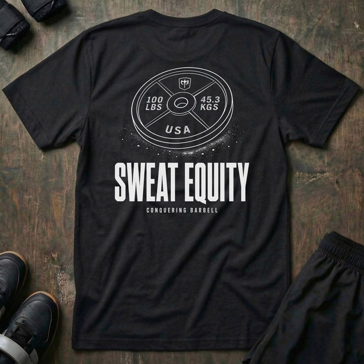 Sweat Equity tee in Black: a 100 lb USA plate with the CB shield and chalk dust scattered at its base