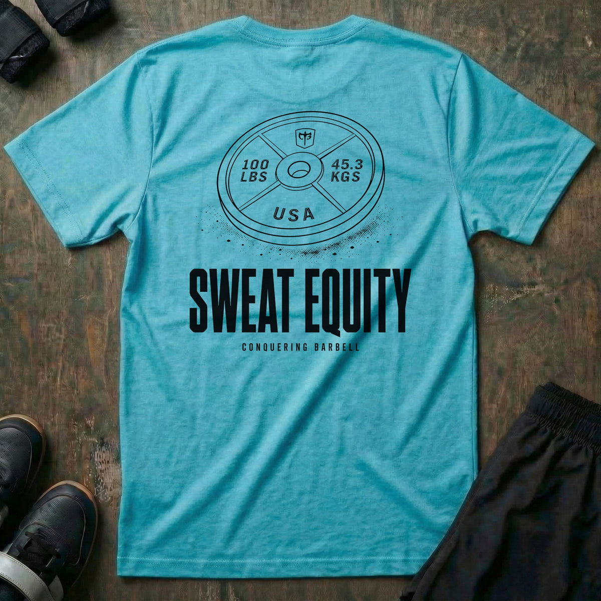 Sweat Equity tee in Tahiti: a 100 lb USA plate with the CB shield and chalk dust scattered at its base
