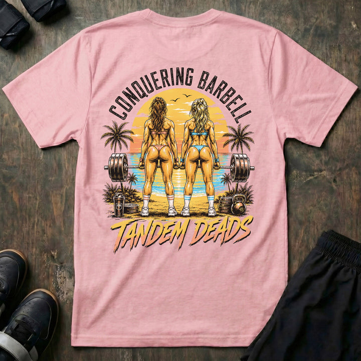 Tandem Deads tee in Pink: two athletic women deadlifting side by side on a palm-lined beach at sunset
